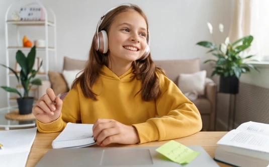 "Uśmiechnięta dziewczynka siedzi przed komputerem, skupiając się na indywidualnej lekcji online w Tutore.